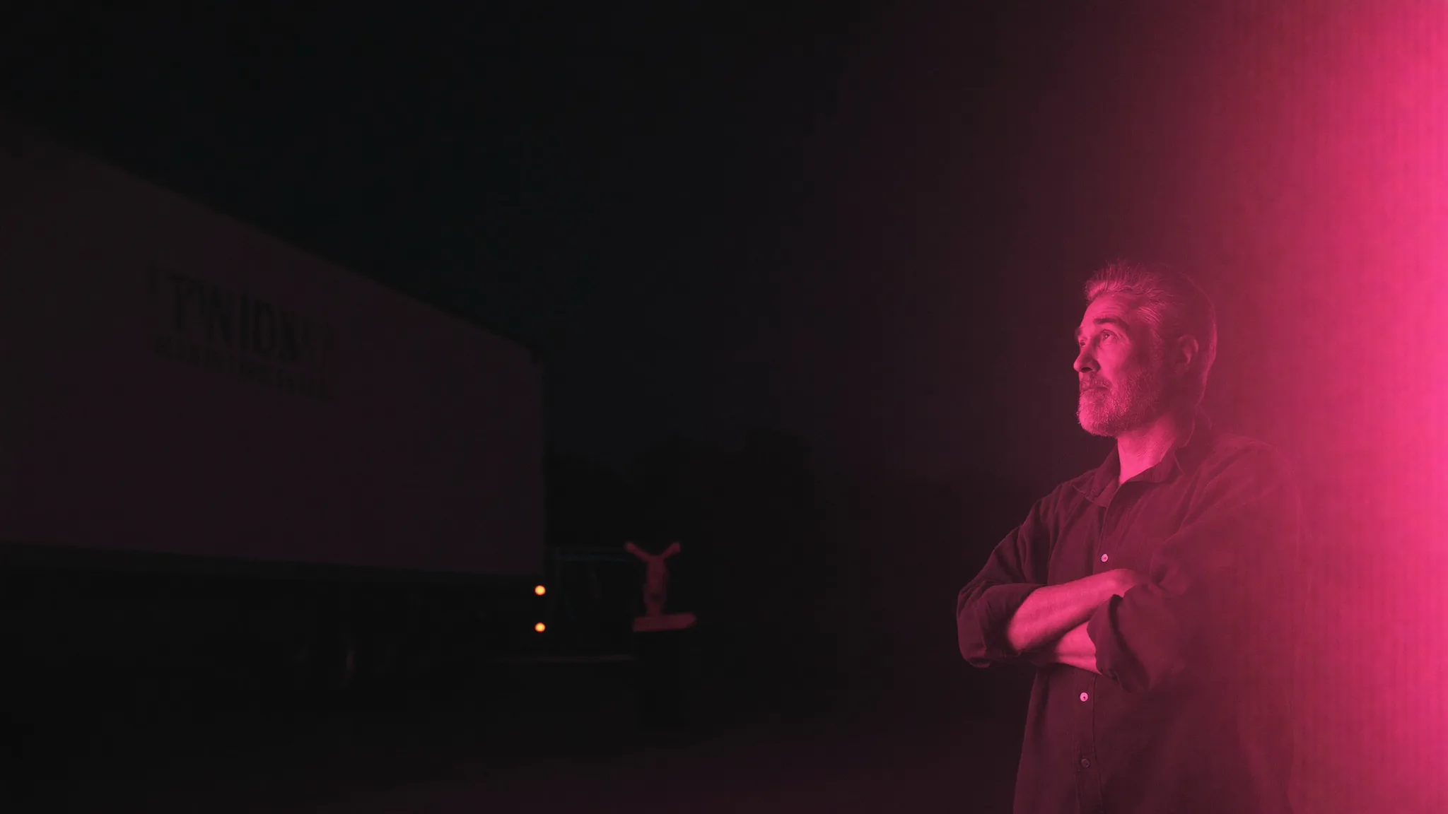 A trade business owner standing in a truck yard at night, lit in magenta