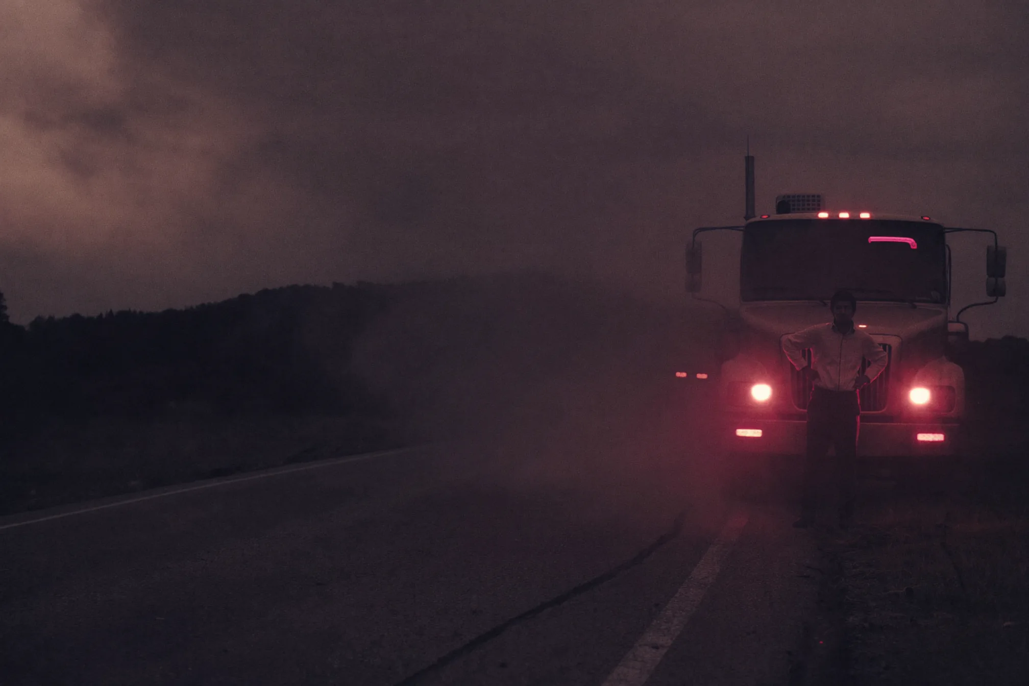 An HVAC technician standing beside his truck on an empty road at dusk