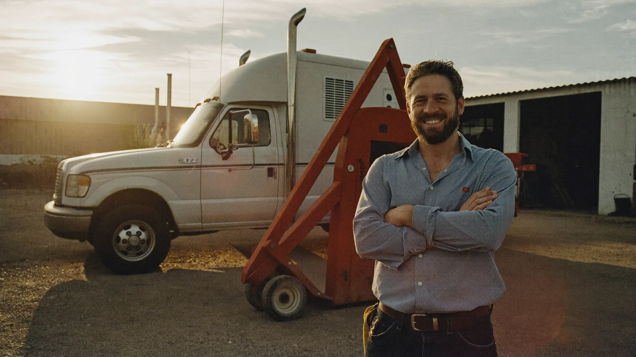 A plumbing business owner standing arms crossed beside his service truck at golden hour