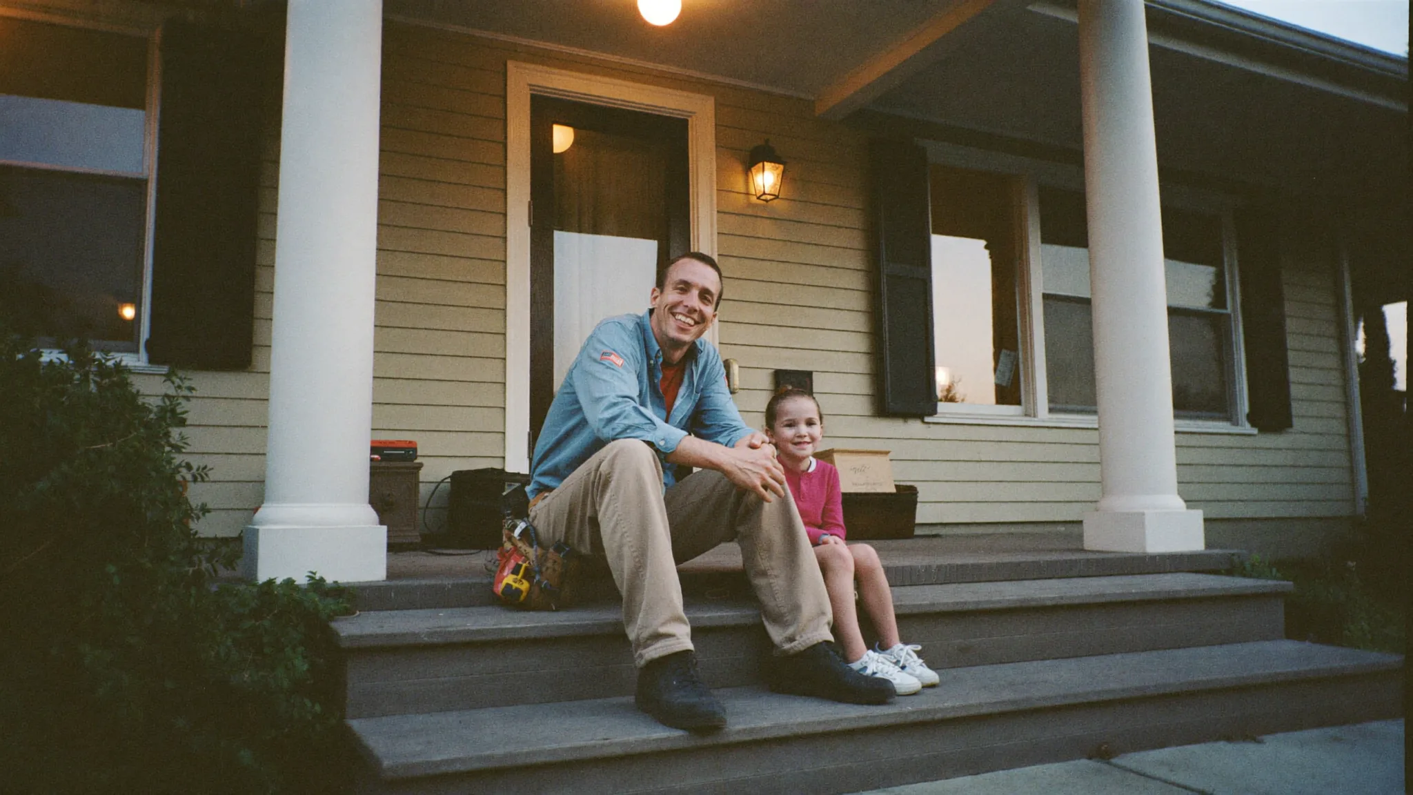 An electrical contractor sitting on his porch steps with his young daughter