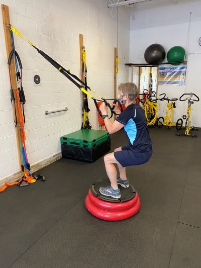 Squatting on a BOSU while holding the TRX straps