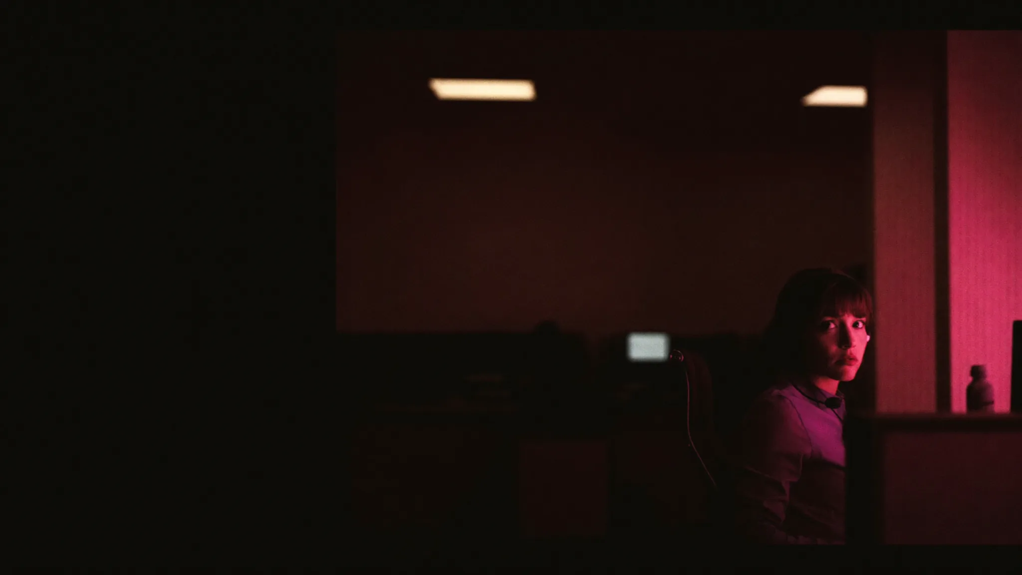 A dispatcher wearing a headset in a dim office, lit in magenta