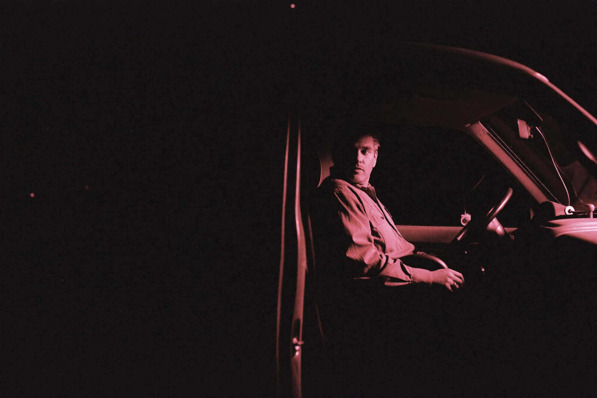 A plumbing contractor sitting alone in a dark service van at night, phone face down beside him